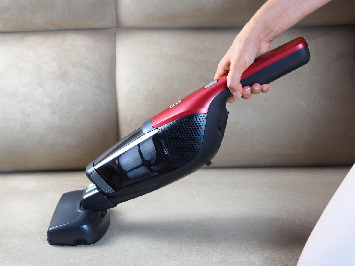 Una persona pasa la aspiradora de mano por su sofá.