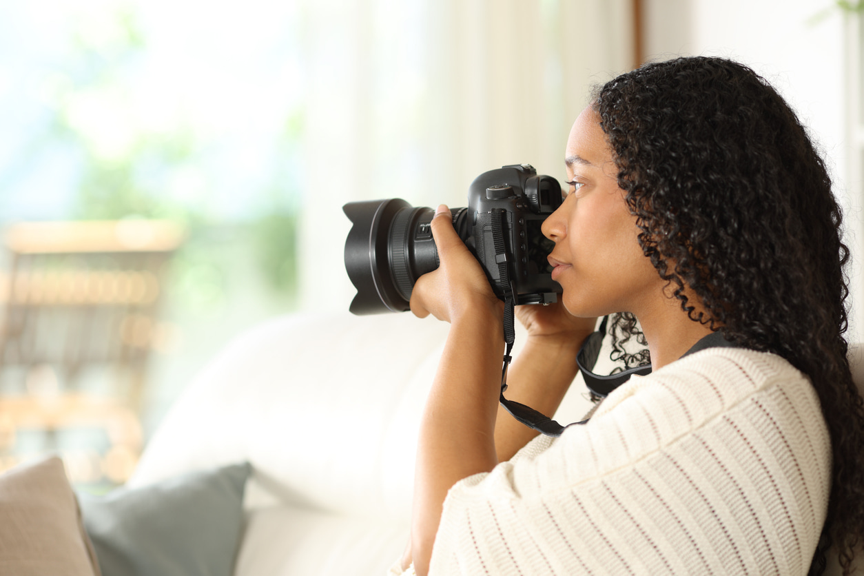 Una mujer hace fotos con su cámara réflex del exterior de su casa desde el sofá.