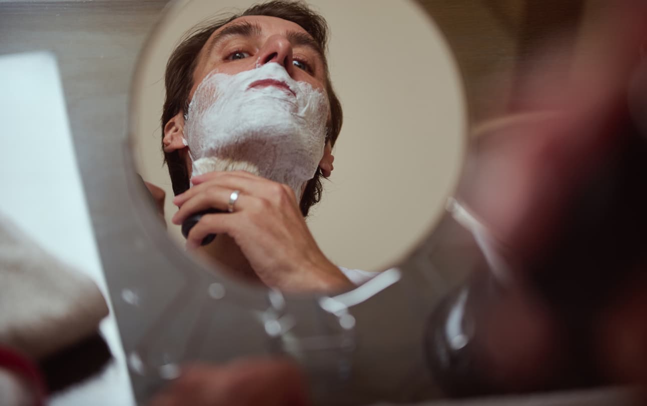 Un hombre se afeita delante del espejo con una maquinilla de BaByliss.